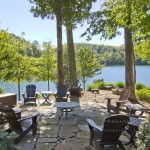 a group of chairs and tables on a stone patio with trees and water in the background